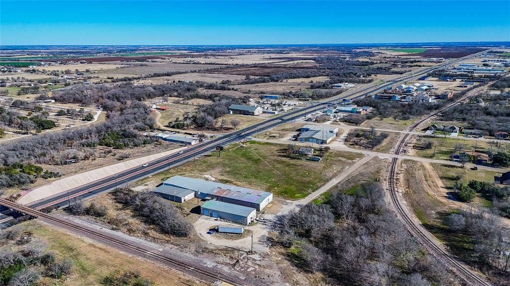 110 1st Street, McGregor, TX 76657 Aerial view of a commercial property featuring multiple metal warehouse structures, paved apron, and direct frontage to a major highway and rail line