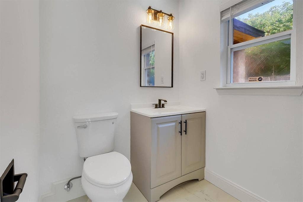 1913 Sandra Kay Lane, Arlington, TX 76015 Vanity cabinet with a white countertop and rectangular sink, matte black hardware, wall-mounted mirror, three-light fixture, and ceramic flooring