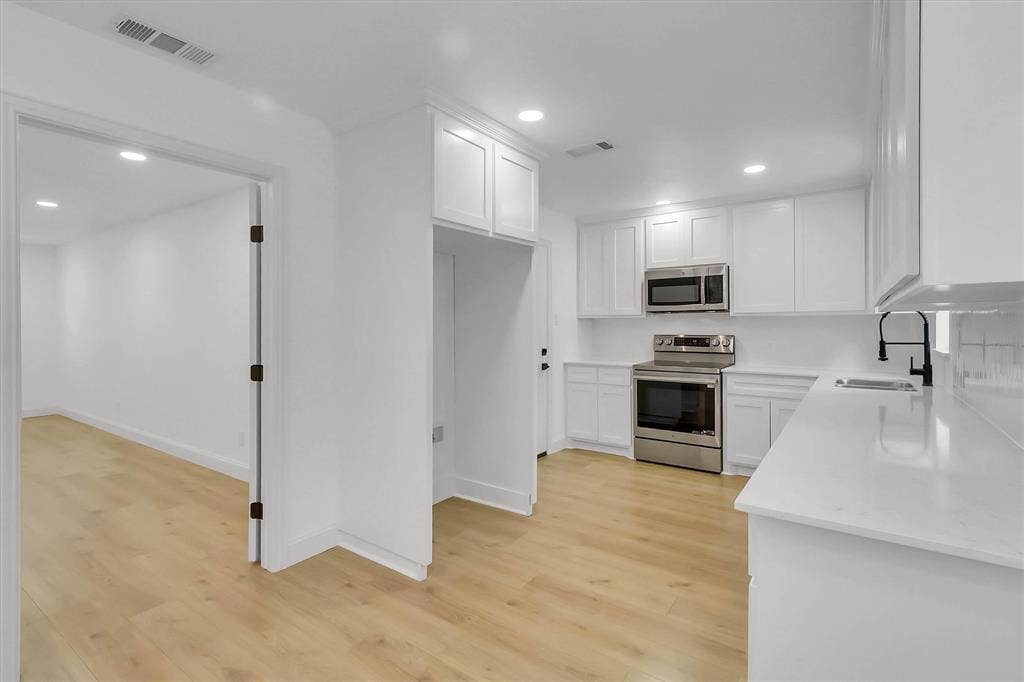 1913 Sandra Kay Lane, Arlington, TX 76015 Kitchen featuring white shaker-style cabinetry, solid-surface countertops, stainless steel appliances, matte black plumbing fixtures, and wood-finish flooring