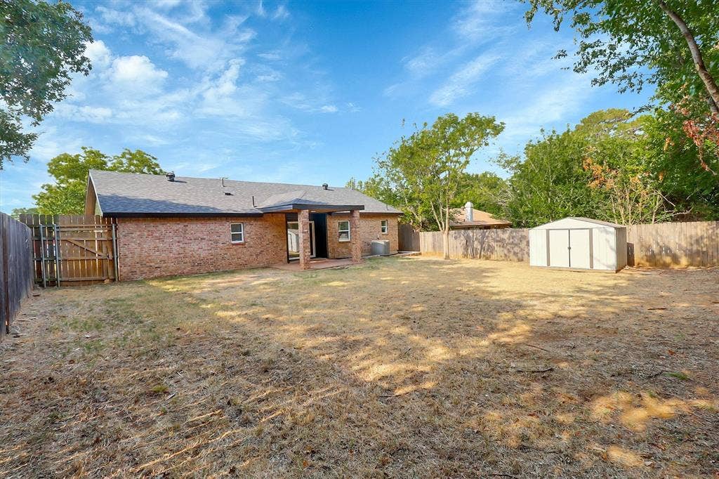 1913 Sandra Kay Lane, Arlington, TX 76015 Brick exterior with a covered rear patio, wood-slat privacy fencing, and a detached storage shed