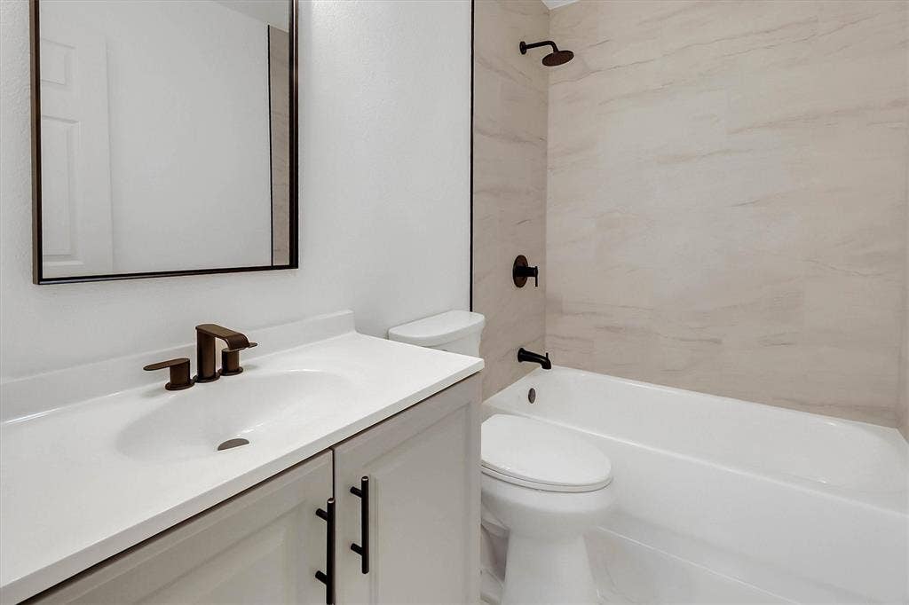 1913 Sandra Kay Lane, Arlington, TX 76015 Bathroom featuring a white vanity cabinet with matte black hardware, a rectangular framed mirror, a porcelain tub surround with neutral-toned tile, and matte black plumbing fixtures
