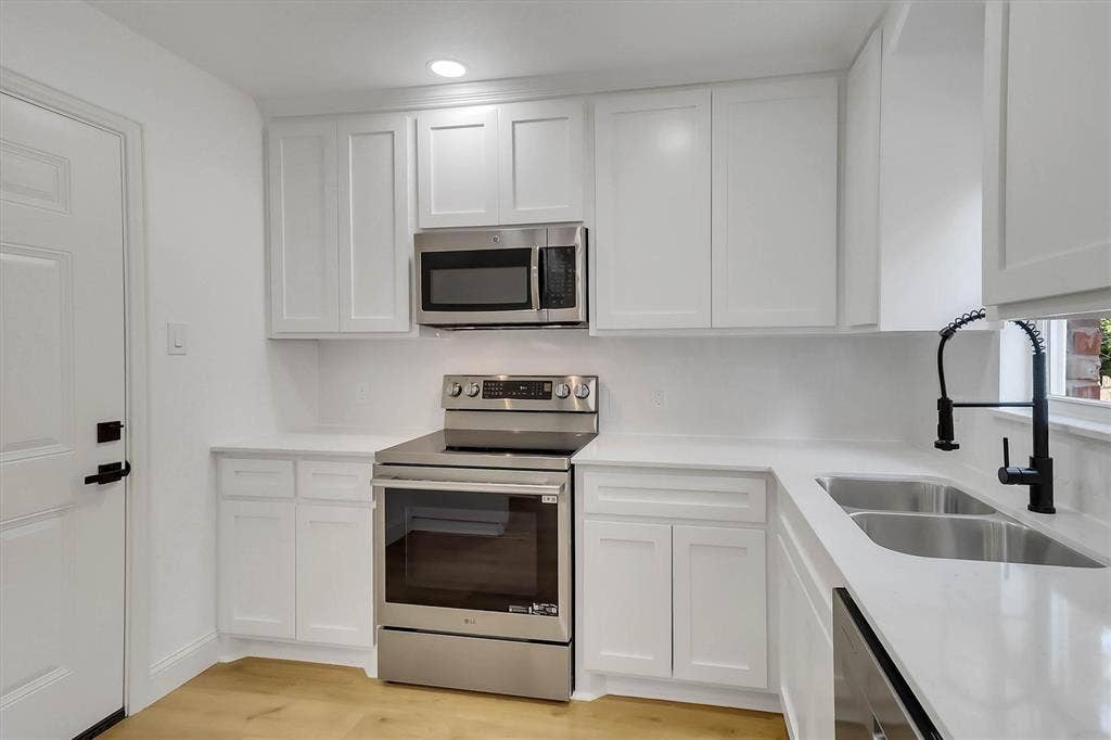 1913 Sandra Kay Lane, Arlington, TX 76015 Kitchen featuring white shaker-style cabinetry, solid-surface countertops, stainless steel appliances, dual-basin sink with a matte black pull-down faucet, and wood-finish flooring