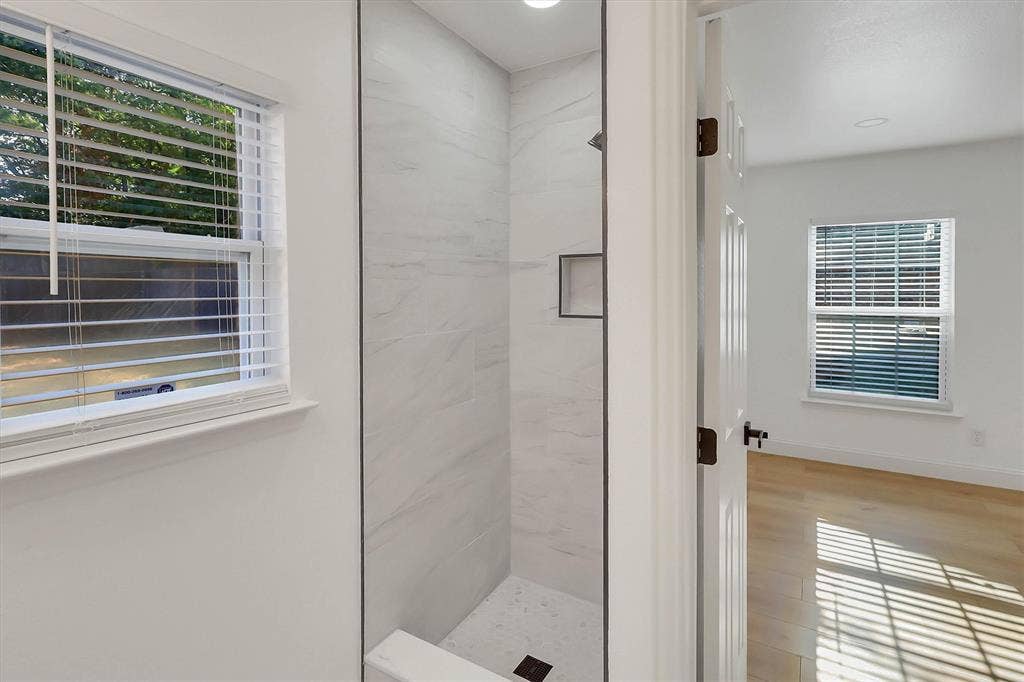 1913 Sandra Kay Lane, Arlington, TX 76015 Walk-in shower featuring large-format stone-patterned tile, integrated recessed shelving, and a custom stone shower pan, complemented by wood-finish flooring and energy-efficient windows