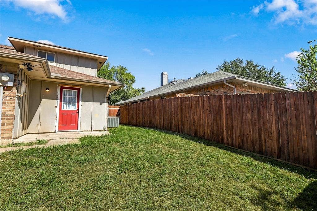 2145 Willow Place, #A, Carrollton, TX 75006 Rear exterior featuring a red entry door, horizontal wood-panel fencing, a concrete patio, and a grass lawn