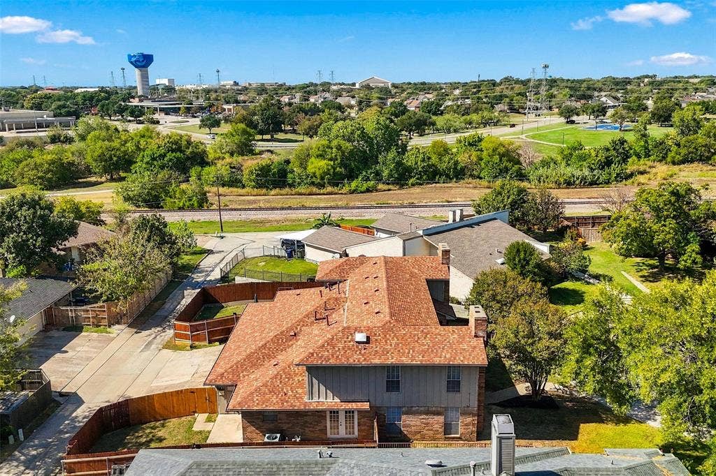 2145 Willow Place, #A, Carrollton, TX 75006 Aerial perspective of a multi-level structure featuring a multi-pitched composition shingle roof, brick and vertical siding exterior, wood-fenced perimeter, and dual masonry chimneys