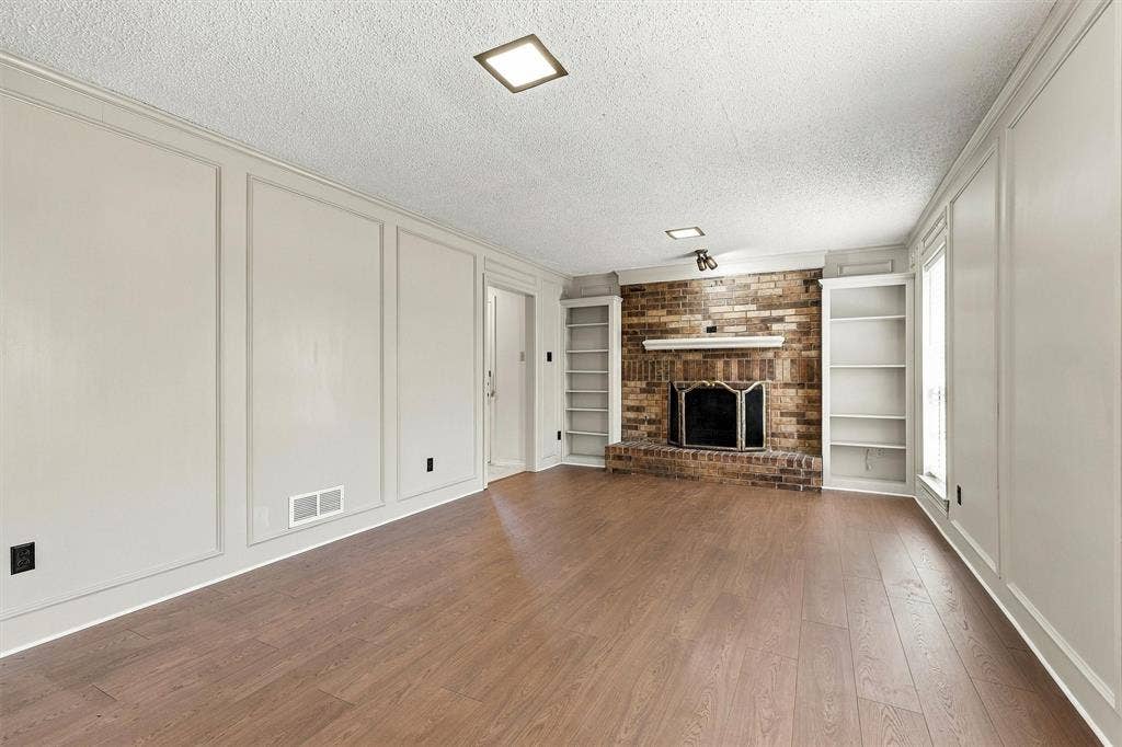 2145 Willow Place, #A, Carrollton, TX 75006 Living space featuring wood-finish flooring, floor-to-ceiling wainscoting, brick fireplace with a mantle, and built-in shelving