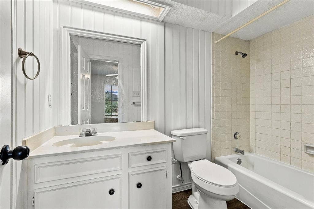 2145 Willow Place, #A, Carrollton, TX 75006 Bathroom featuring vertical plank wall paneling, a white vanity with an integrated sink, a framed mirror, a skylight, and a tiled shower surround