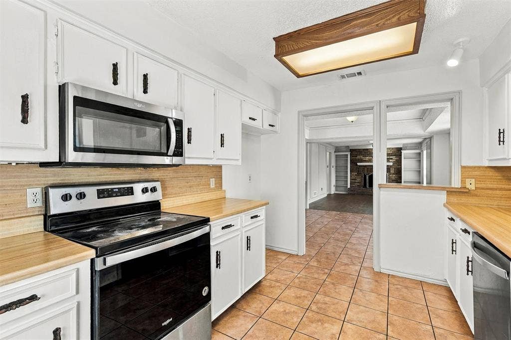 2145 Willow Place, #A, Carrollton, TX 75006 Kitchen featuring white cabinetry, wood-finish countertops, stainless steel appliances, tile flooring, and integrated overhead lighting