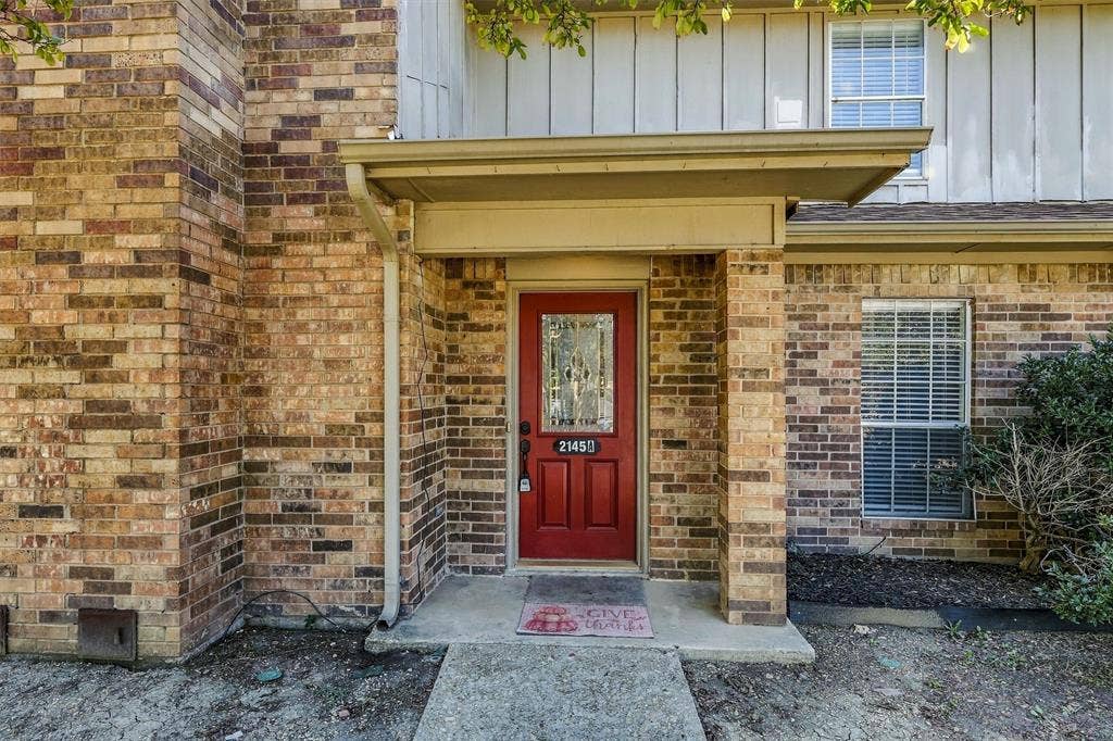 2145 Willow Place, #A, Carrollton, TX 75006 Exterior facade featuring multi-tonal brick masonry, vertical siding, a covered entryway, and a red front door with a decorative glass insert
