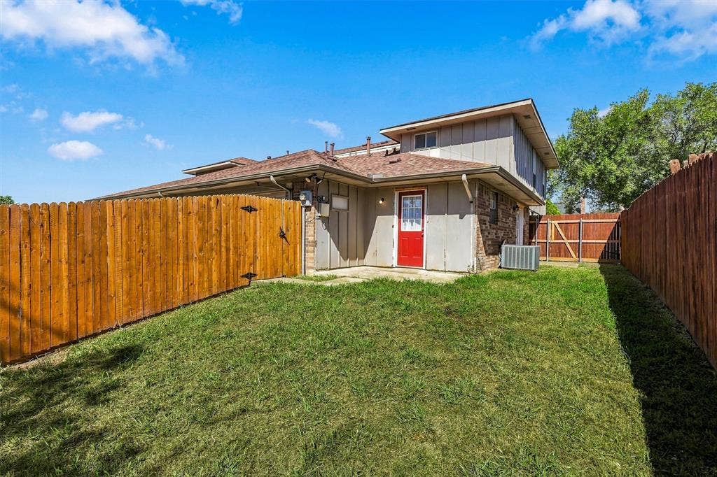 2145 Willow Place, #A, Carrollton, TX 75006 Rear exterior featuring a wood fence, concrete patio, grass lawn, and brick and vertical siding facade