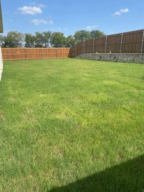 Backyard featuring a grass lawn, full-height wood privacy fencing, and a stone retaining wall