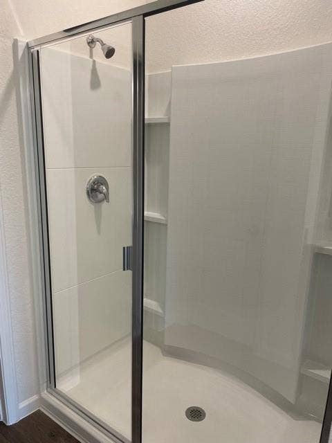 Walk-in shower enclosure featuring a chrome-finished faucet, built-in shelving, a curved glass door, and white surround panels