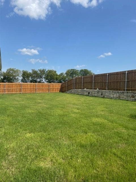 Expansive backyard featuring a level lawn, stone retaining wall, and full-perimeter wood privacy fencing