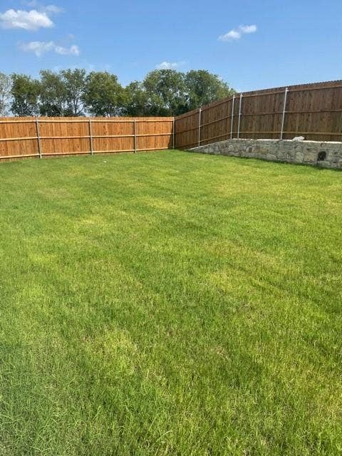 Expansive backyard featuring a leveled grass lawn, wood privacy fencing, and a stone retaining wall