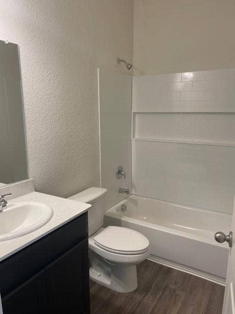 Bathroom featuring a vanity with a light-toned countertop, integrated basin, dark cabinetry, wood-finish flooring, and a tub-shower combination with white wall surround