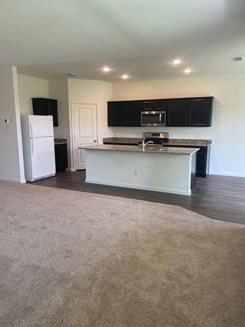 Kitchen featuring dark cabinetry, stone-surface countertops, center island, recessed ceiling lighting, and wood-finish flooring
