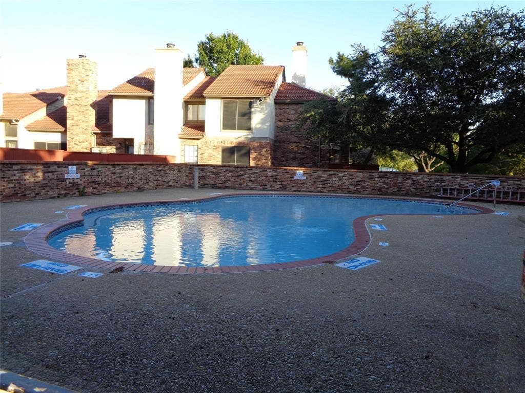 909 Turtle Cove, #141, Irving, TX 75060 In-ground swimming pool featuring a brick-paver perimeter, aggregate decking, and a surrounding brick privacy wall