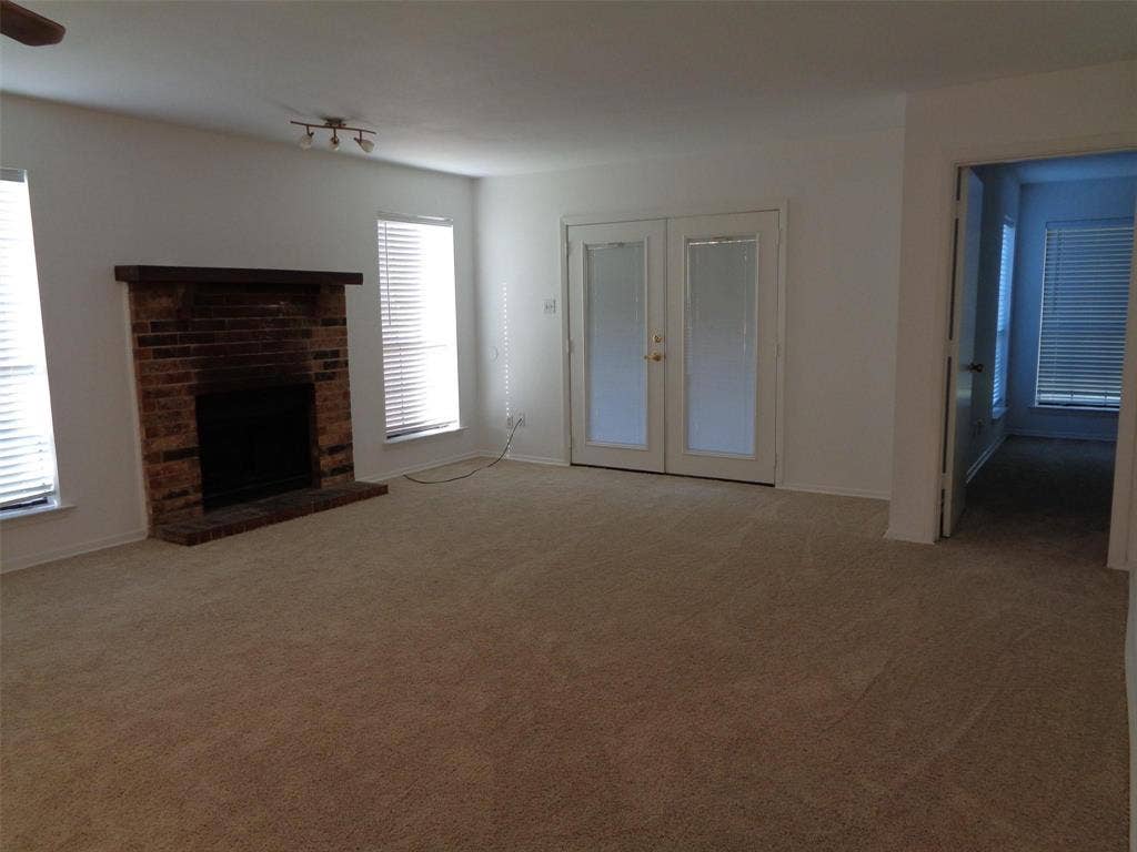909 Turtle Cove, #141, Irving, TX 75060 Living area featuring a full-height masonry fireplace with a timber mantel, neutral carpeting, glass-paned double doors, and natural lighting provided by multiple windows