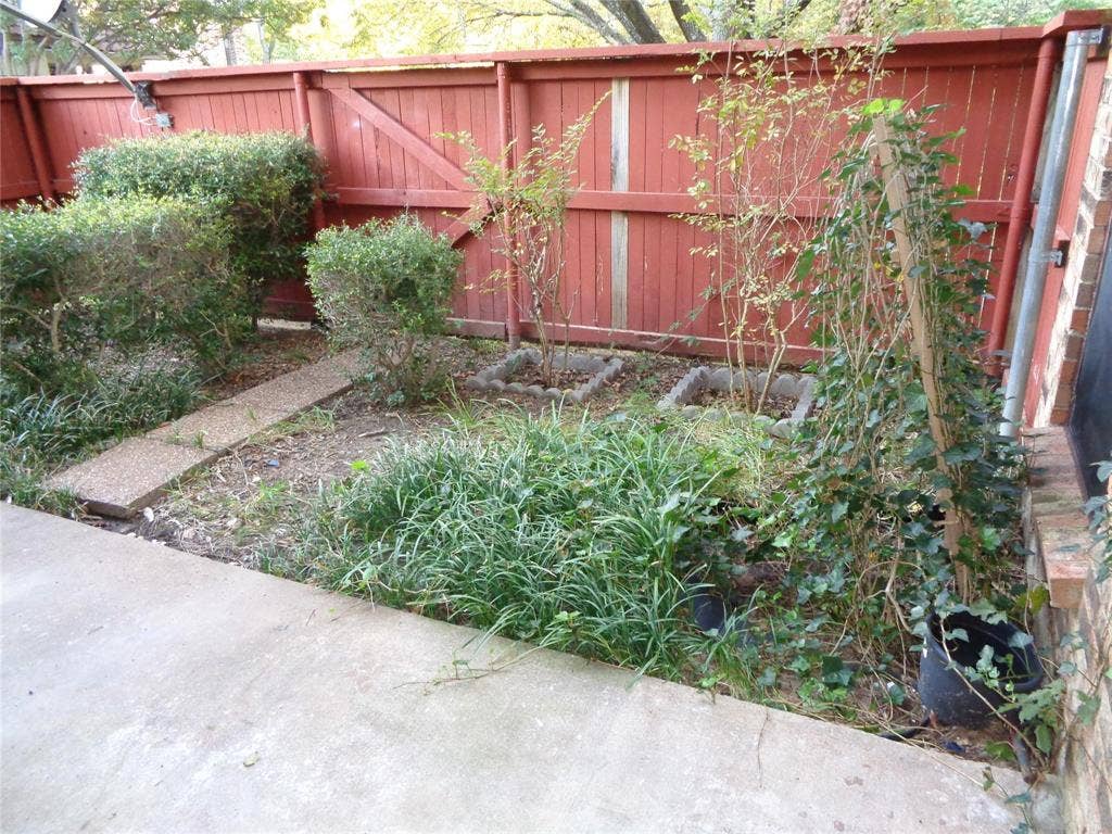 909 Turtle Cove, #141, Irving, TX 75060 Concrete patio area with a wooden privacy fence, mature shrubbery, and stone edging