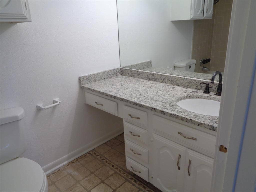 909 Turtle Cove, #141, Irving, TX 75060 Vanity featuring a stone-composite countertop, undermount sink, dark-finish faucet, and white cabinetry with multi-drawer storage, accompanied by a wall-mounted mirror