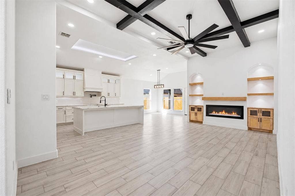 101 Connor Circle, Mabank, TX 75147 Open-concept space featuring vaulted ceilings with exposed wood-finish beams, wood-finish flooring, a linear fireplace with built-in shelving, a kitchen with a center island, and recessed lighting