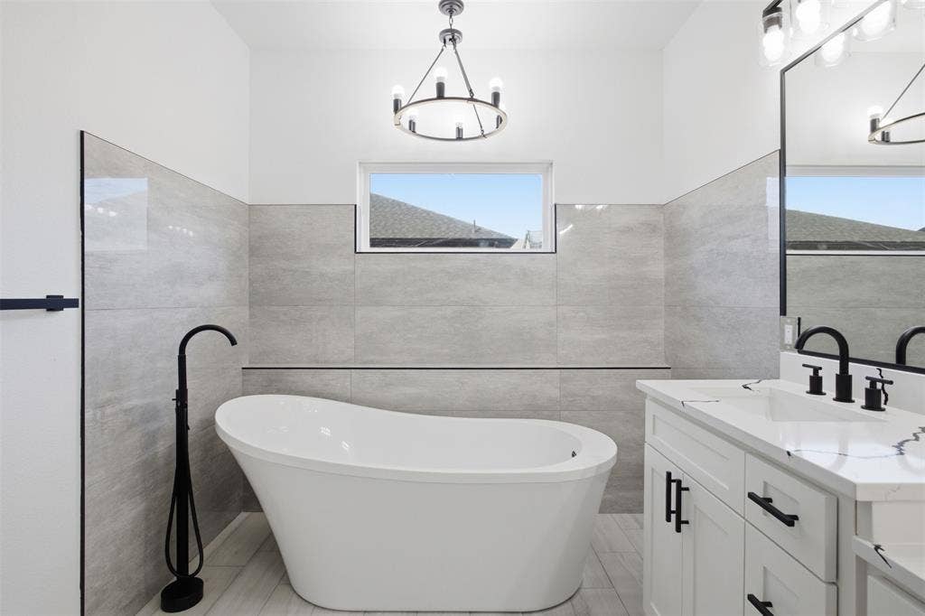 101 Connor Circle, Mabank, TX 75147 Freestanding soaking tub with a floor-mounted matte black faucet, vanity with white cabinetry and a stone-surface countertop, matte black hardware, and large-format gray wall tile