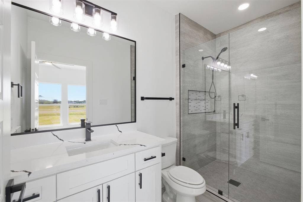 101 Connor Circle, Mabank, TX 75147 Bathroom featuring a white vanity with veined stone-finish countertop, undermount sink, frameless glass-enclosed shower with tile surround, and matte black fixtures