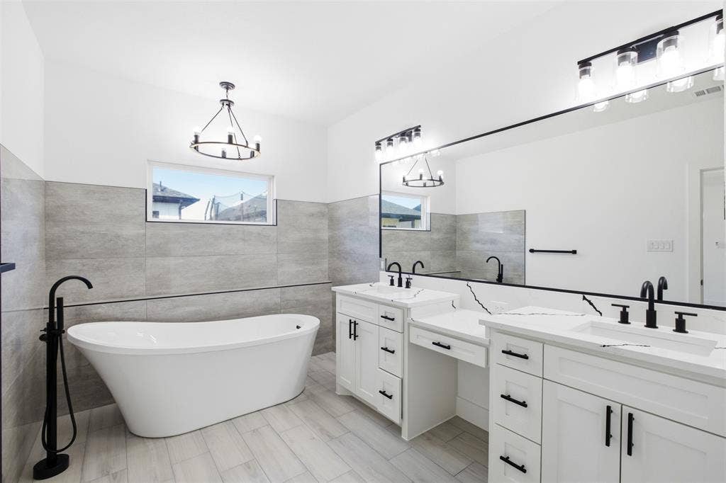 101 Connor Circle, Mabank, TX 75147 Freestanding soaking tub with matte black floor-mounted faucet, dual-sink vanity with white stone-finish countertop, full-width vanity mirror, tile-surround wall detailing, and wood-finish flooring