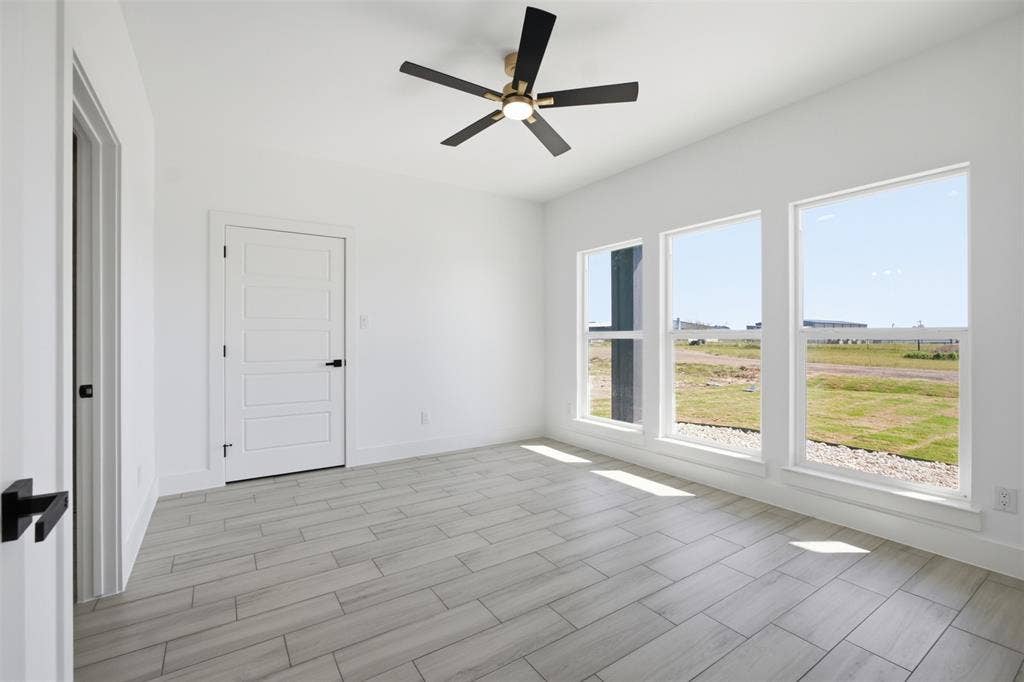 101 Connor Circle, Mabank, TX 75147 Neutral color palette featuring wood-finish flooring, three large windows, a four-panel interior door with matte black hardware, and a ceiling fan with integrated lighting