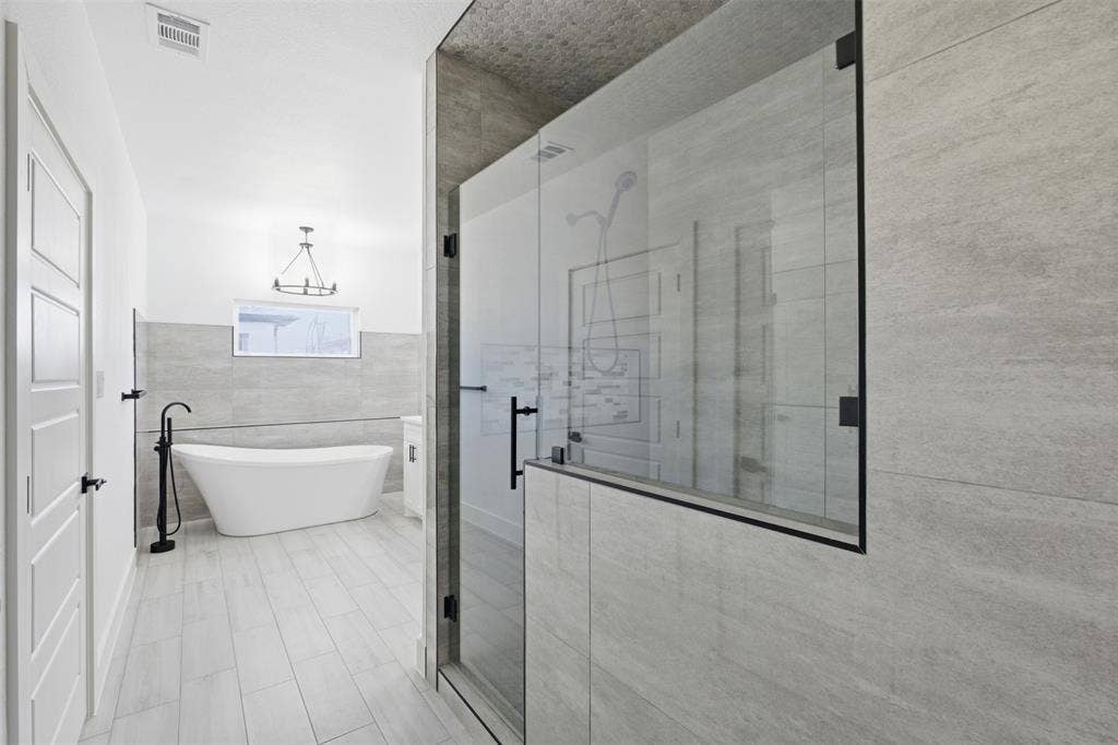 101 Connor Circle, Mabank, TX 75147 Freestanding soaking tub with matte black floor-mounted faucet, walk-in glass-enclosed shower with matte black hardware, and large-format tile wall and floor finishes