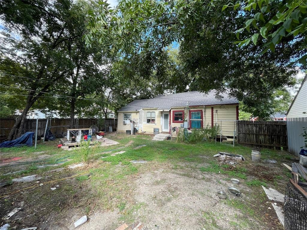 1115 Pine Street, Grand Prairie, TX 75050 Rear exterior featuring horizontal lap siding, a shingled roof, mature trees, and wooden perimeter fencing