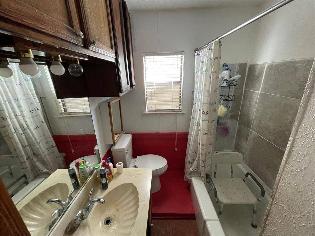 1115 Pine Street, Grand Prairie, TX 75050 Bathroom featuring a molded shell-design sink, wood-finish cabinetry, a large wall-mounted mirror, and tile-surround bathtub
