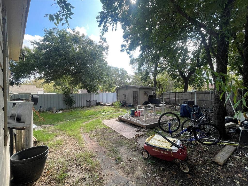 1115 Pine Street, Grand Prairie, TX 75050 Backyard featuring mature trees, a detached storage structure, and a brick-paved pathway enclosed by perimeter fencing