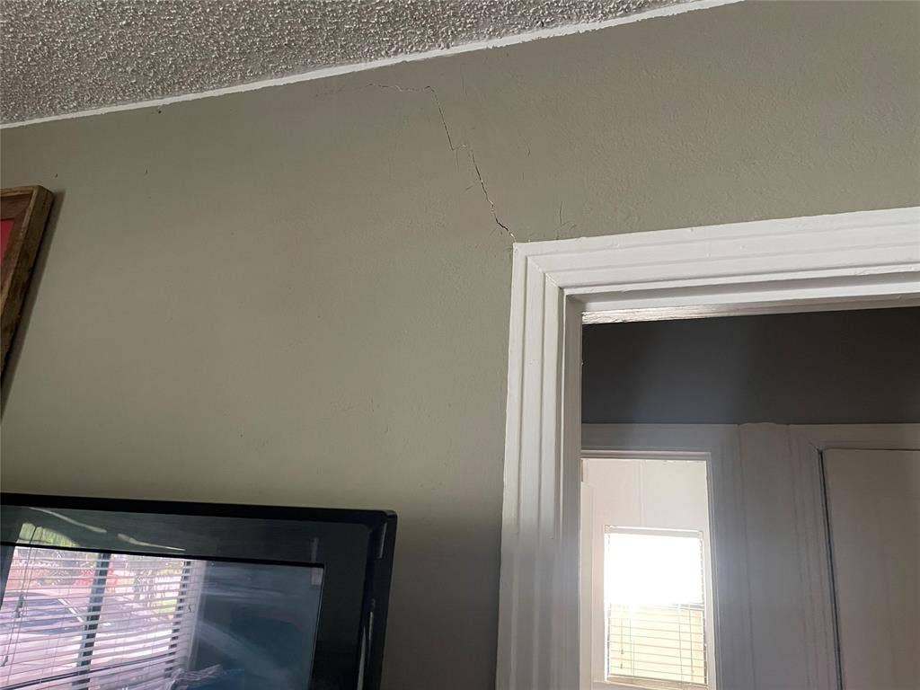 1115 Pine Street, Grand Prairie, TX 75050 Painted drywall surface with visible vertical fissure extending from the corner of a white-cased doorway featuring decorative molding and a popcorn-textured ceiling