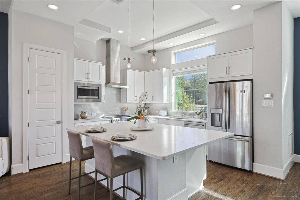 Kitchen featuring wall chimney range hood, a center island, white cabinetry, stainless steel appliances, and dark wood-type flooring