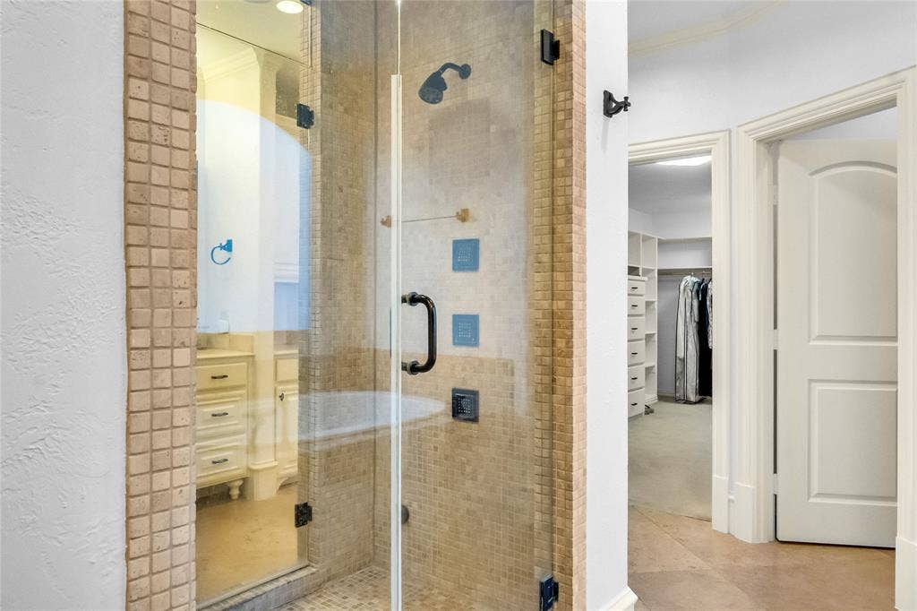 Walk-in shower featuring a glass door, stone-tile surround, and wall-mounted showerhead, accompanied by built-in closet cabinetry