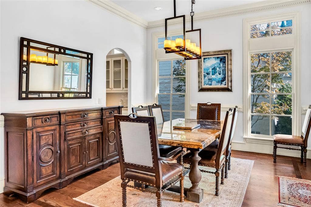 Dining area featuring wood-finish flooring, floor-to-ceiling windows with transom detailing, crown molding, and a rectangular multi-light pendant chandelier