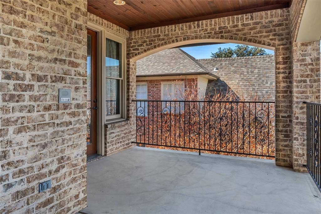 Covered balcony featuring an arched brick exterior, exposed wood-plank ceiling, and decorative wrought-iron railing