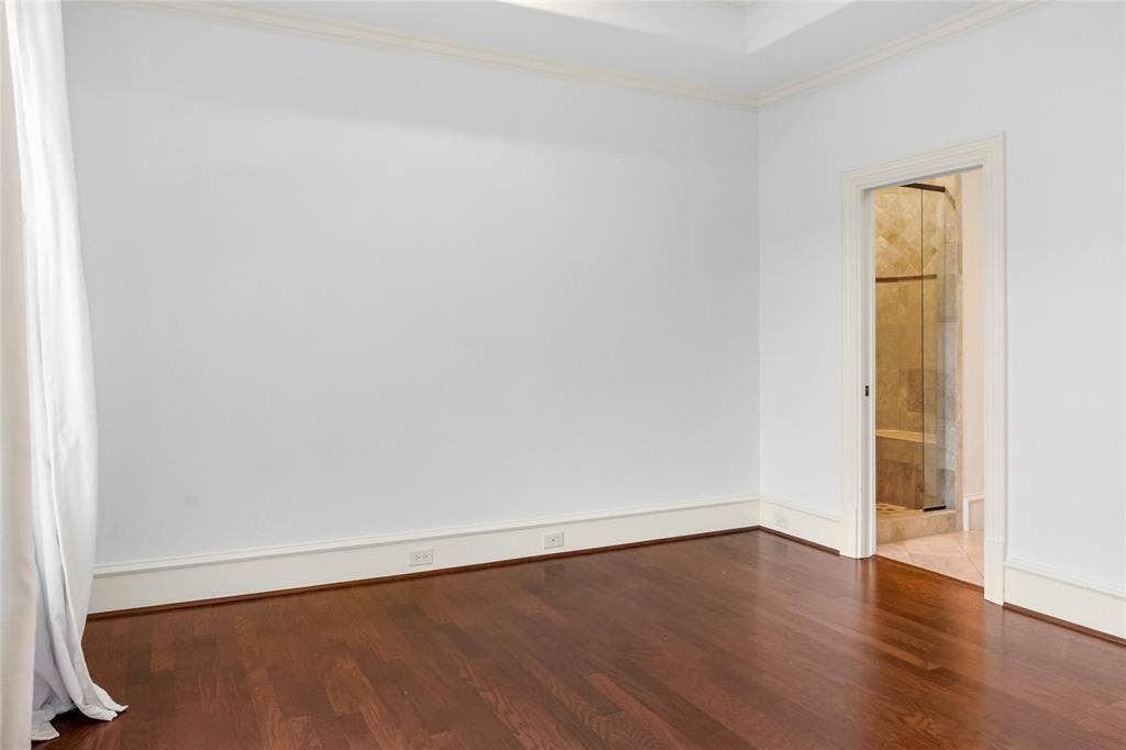 Room featuring wood-finish flooring, a tiered tray ceiling, and crown molding, with an entry to a tiled shower space
