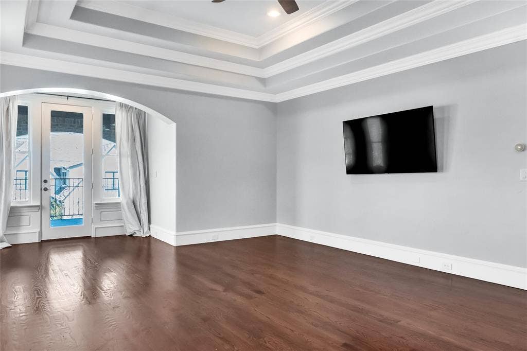 Tray ceiling, wood-finish flooring, arched doorway, and glass-paneled door