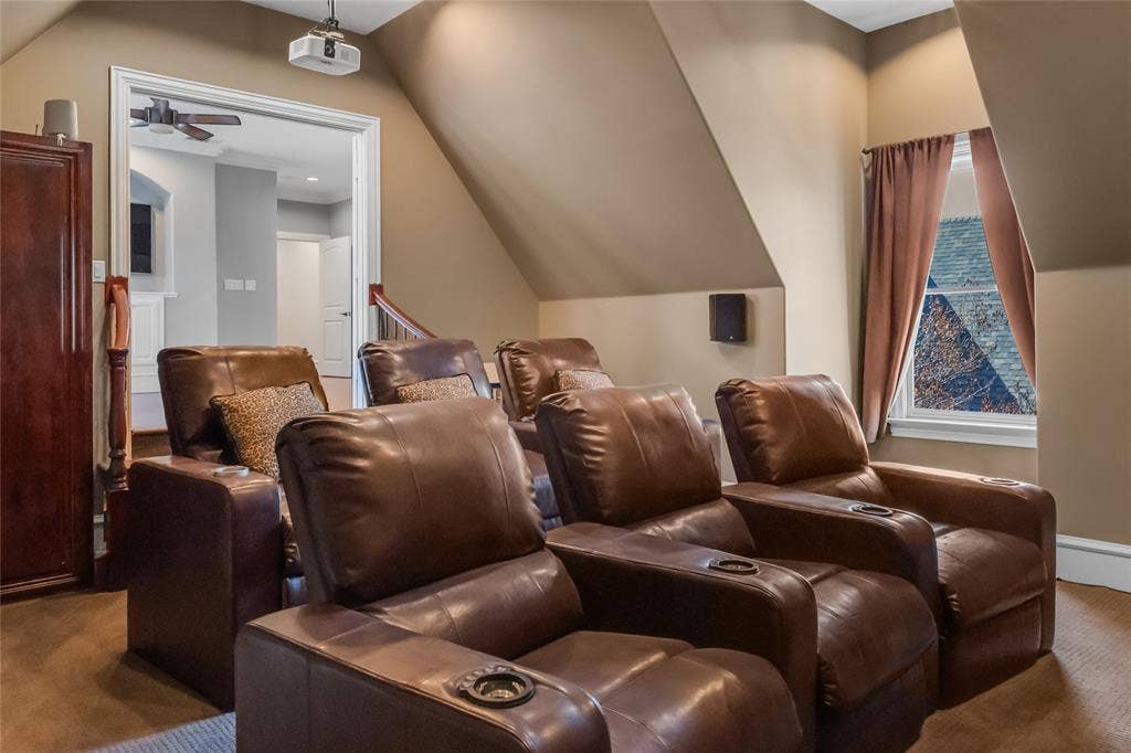 Vaulted ceiling with angled walls, carpeted flooring, wall-mounted speakers, ceiling-mounted projector, and window with casing