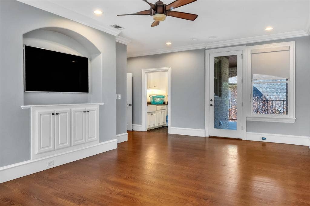 Hardwood flooring, arched recessed media alcove with custom cabinetry, crown molding, and recessed lighting