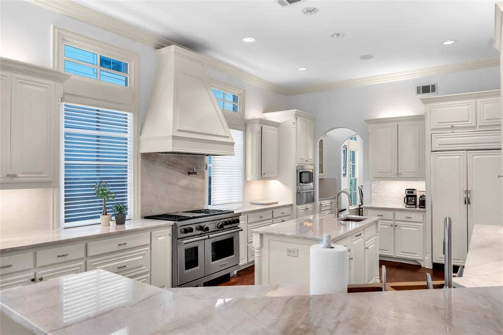 Kitchen featuring custom cabinetry, a stone-surround range hood, a stainless steel gas range, stone countertops, and a center island with an integrated sink