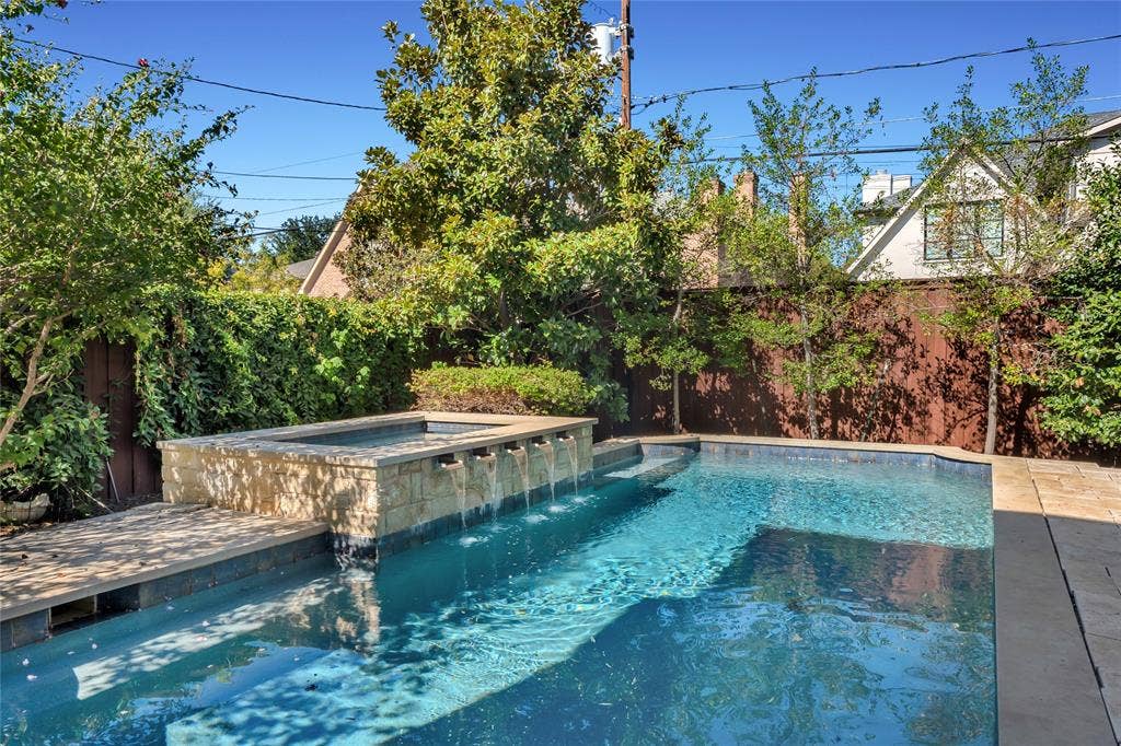 Backyard pool featuring a spillover spa, stone-veneer accent wall, water features, and natural stone decking