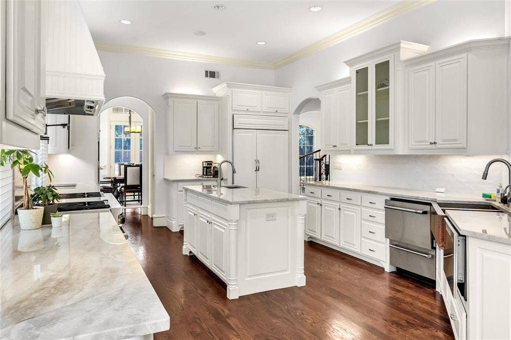 Kitchen featuring white cabinetry, stone countertops, a center island with an integrated sink, stainless steel appliances, and wood-finish flooring