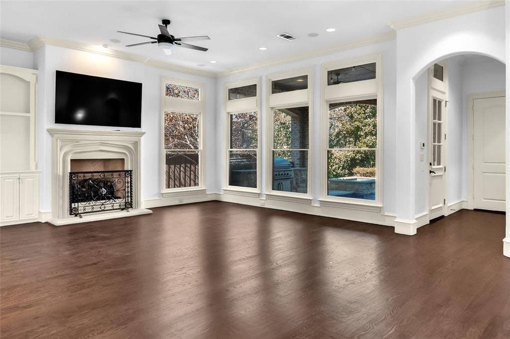 Living area featuring wood-finish flooring, tall windows, a built-in stone-surround fireplace, arched architectural detailing, and custom built-in cabinetry