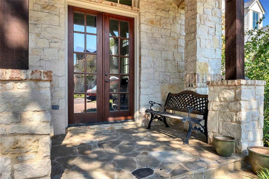 Covered porch featuring flagstone flooring, natural stone veneer columns, and glass-paneled double entry doors