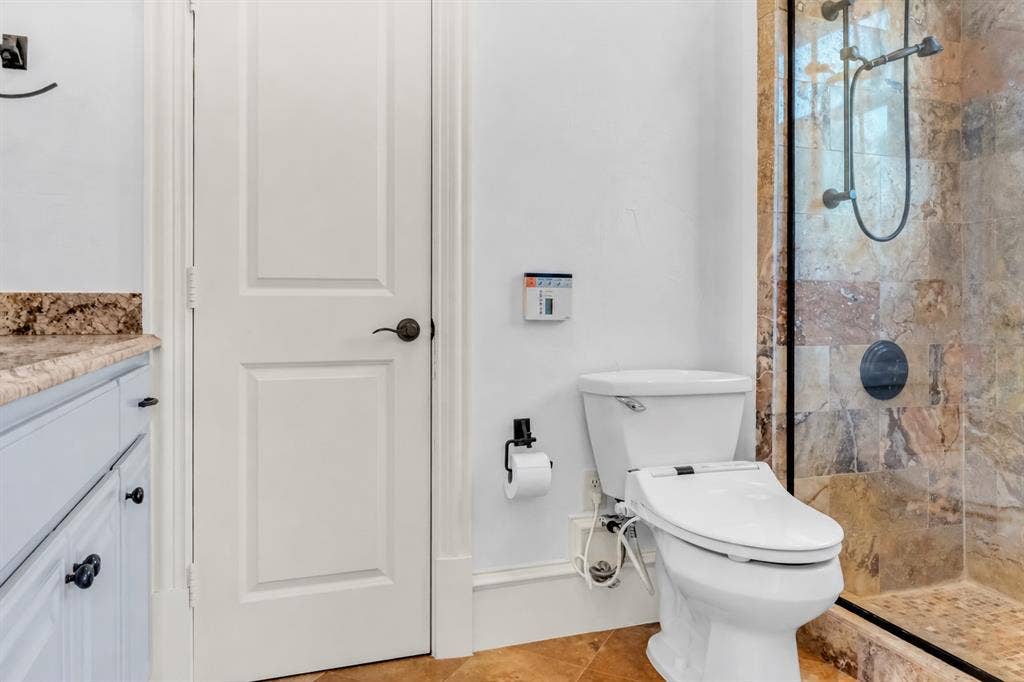 Bathroom featuring a walk-in shower with stone tile surround, natural stone flooring, vanity with stone countertop, and matte black hardware