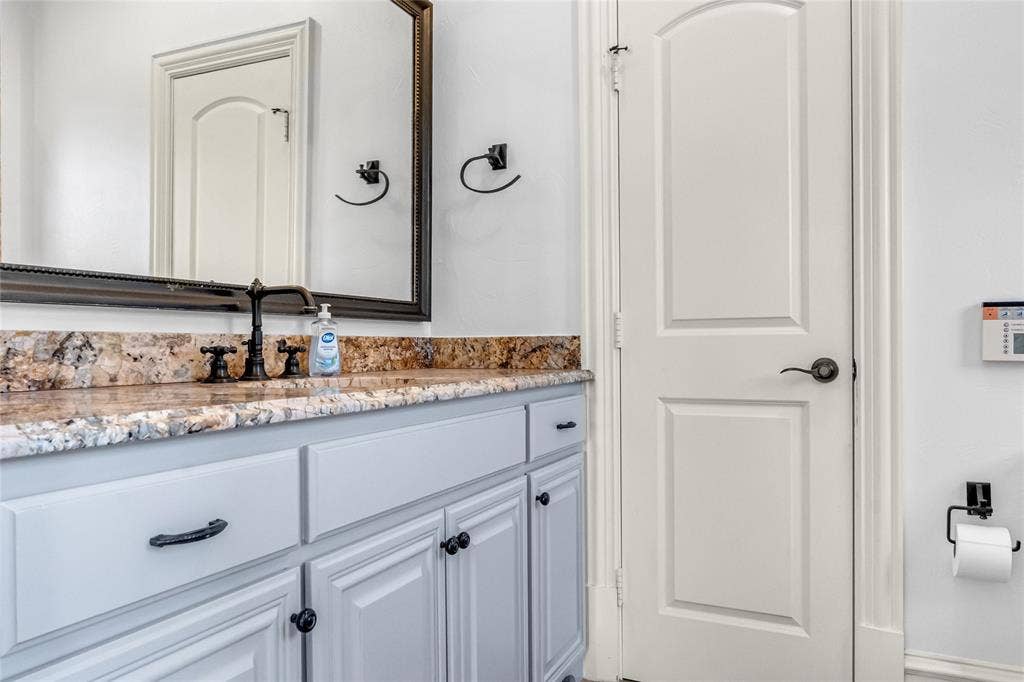 Vanity featuring a stone-surface countertop, dark-finish widespread faucet, and paneled cabinetry with matte black hardware, paired with a framed wall-mounted mirror