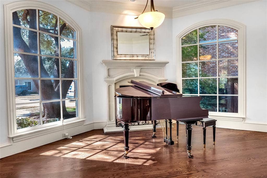 Wood-finish flooring, fireplace with a custom stone surround, two oversized arched windows with muntin detailing, and a pendant light fixture